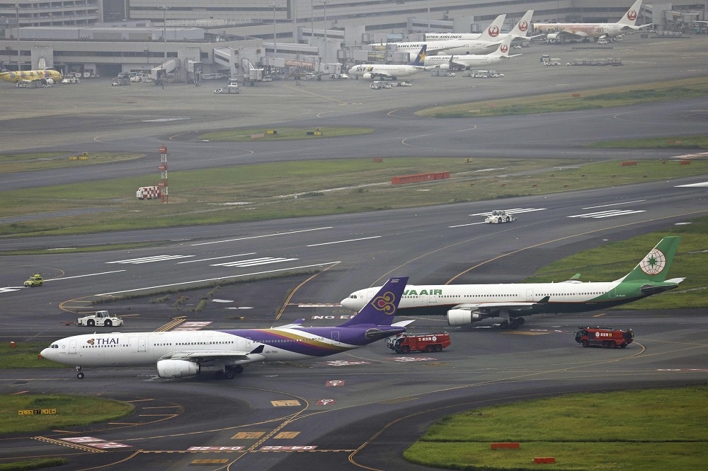 長榮航空與泰航班機在羽田機場發生擦撞後，由地面人員引導至定位暫時停放。（美聯社）