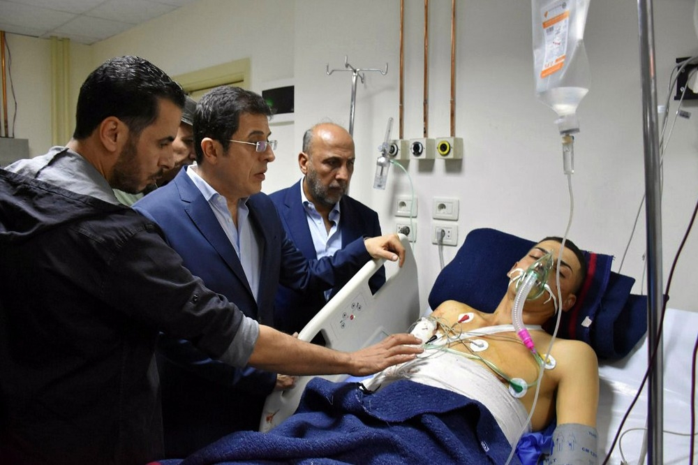 敘利亞1間軍校5日遭無人機襲擊，衛生部長加巴什（中）正在慰問傷者。（美聯社）